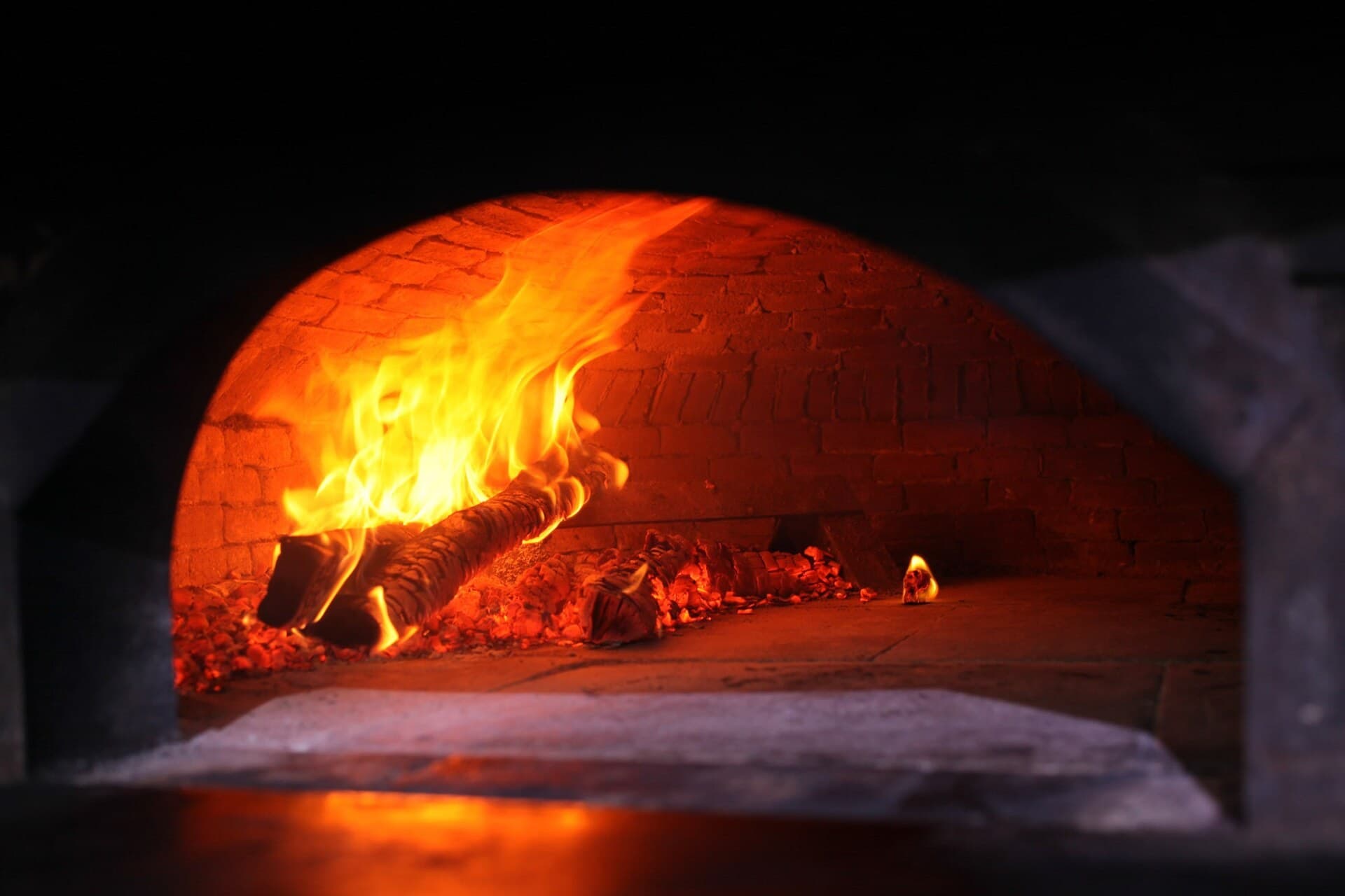 Wood fire burning inside a brick pizza oven dome, lighting the oven floor