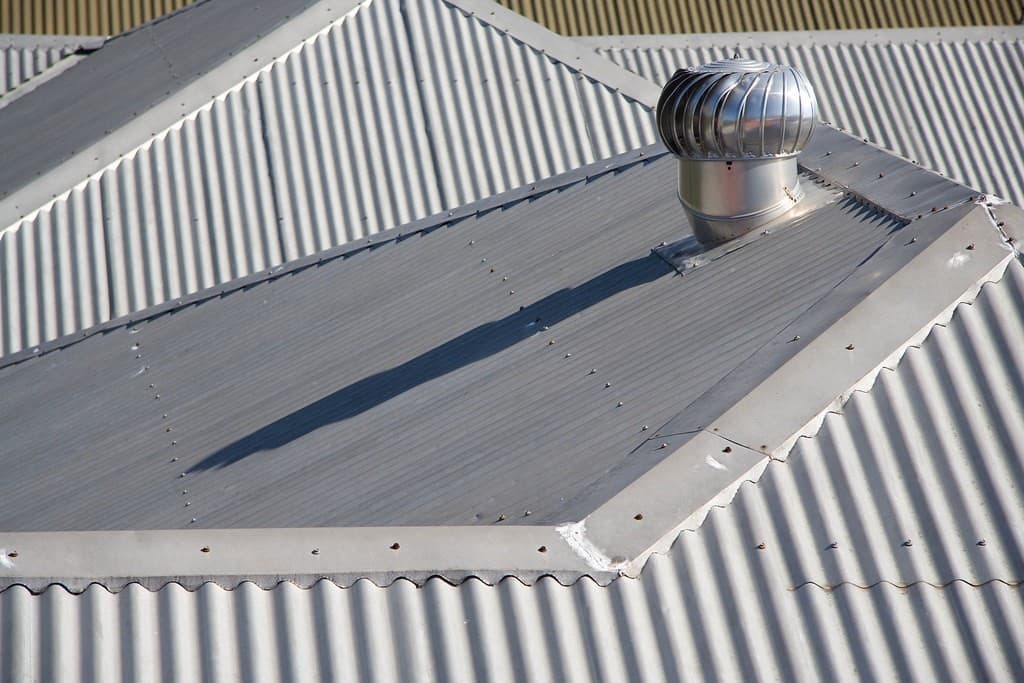 A shiny turbine roof cyclone fitted on a corrugated metal roof with a sealed flashing base